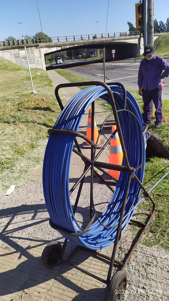 Rollo de guía pasacables junto a una cámara subterránea abierta durante un tendido de fibra óptica bajo un paso bajo nivel