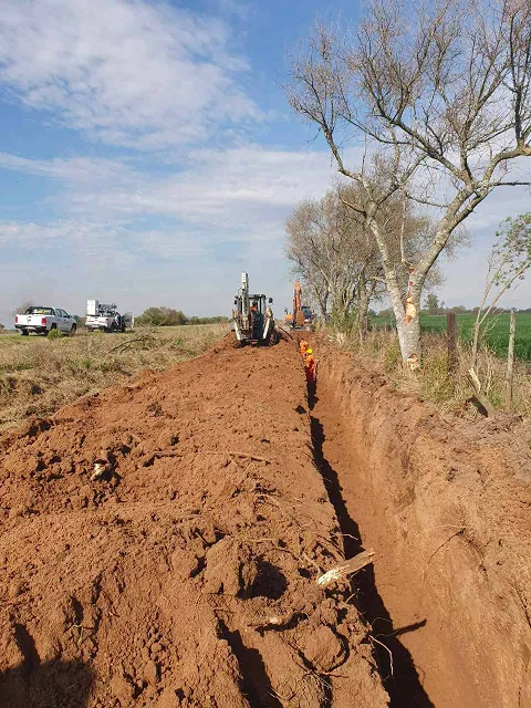 Zanja abierta con retroexcavadora para el tendido subterráneo de fibra óptica en zona rural