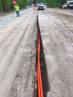 Tritubo naranja colocado en zanja al costado de la calzada para el tendido subterráneo de fibra óptica